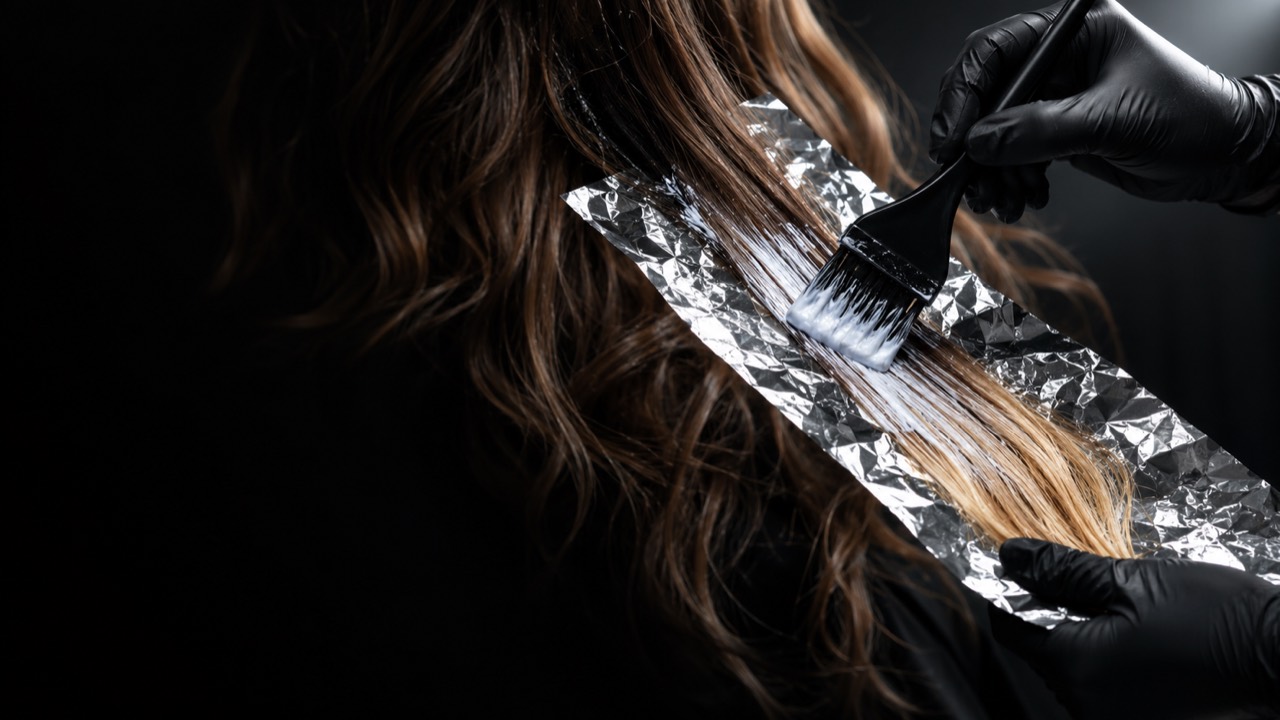 Pensula întinde decolorantul pe o șuviță așezată pe folie, la un balayage