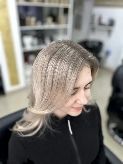 Clientă cu păr blond deschis cu reflexe, coafat lejer, în salon